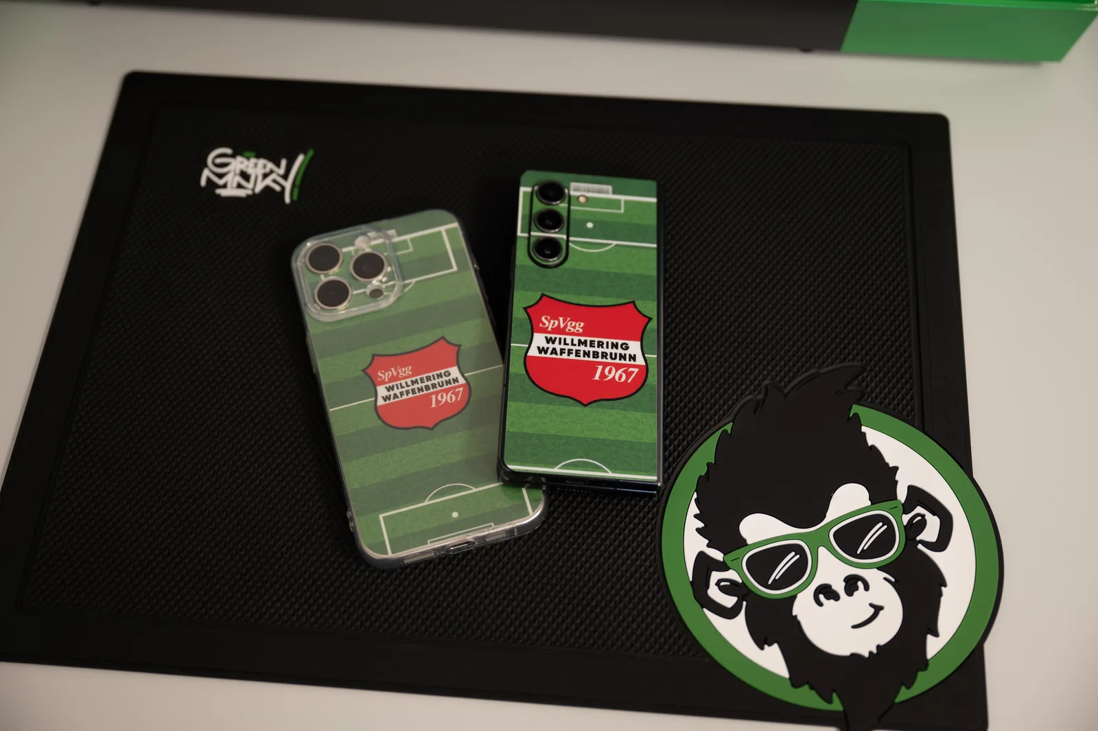 Zwei Smartphones mit individuell gestaltetem Backcover im Vereinsmotiv der SpVgg Willmering Waffenbrunn auf einer GREENMNKY-Schneidematte
