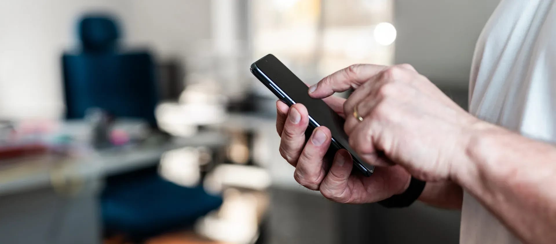 Person hält ein Smartphone in der Hand und bedient es in einem Büro
